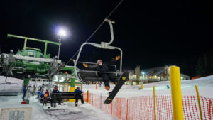 A person on a chairlift at Snow Valley in Edmonton smiling and cheering with arms raised during a festive winter holiday event.